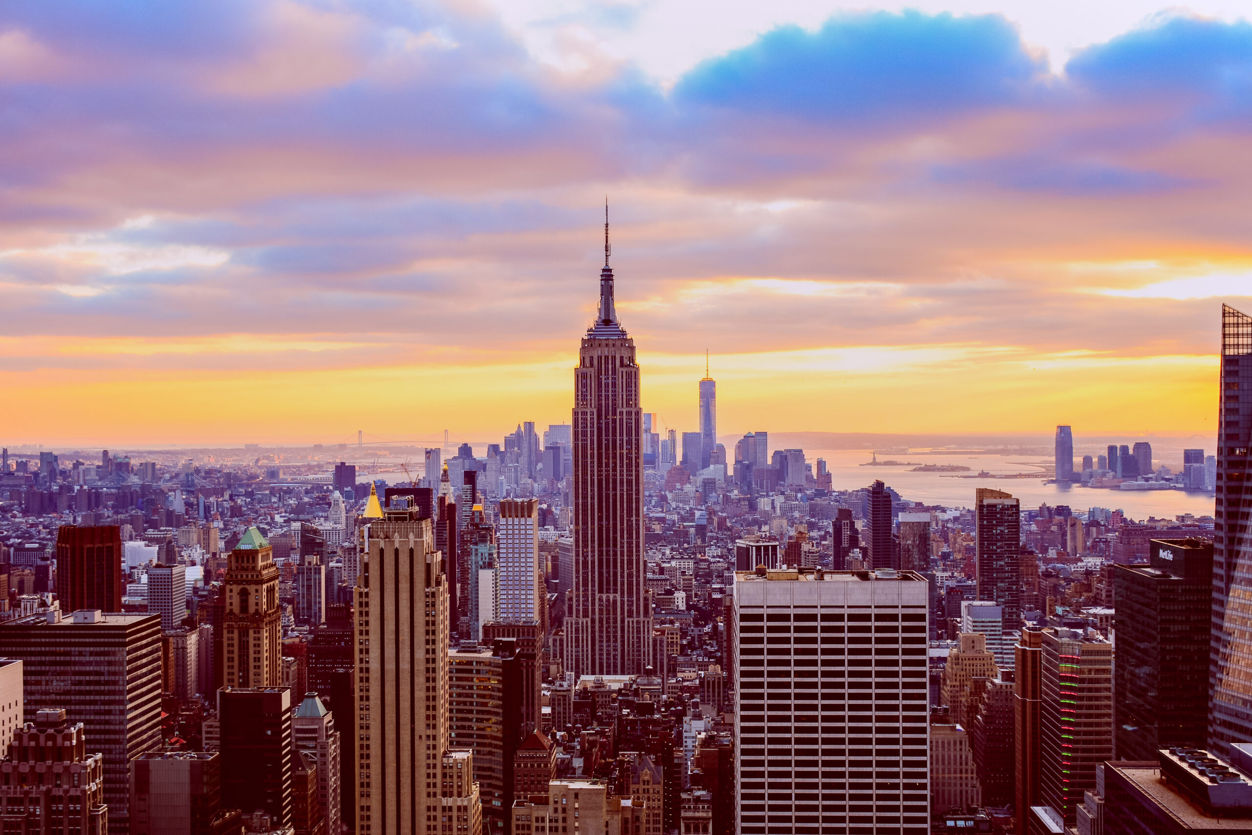 A classic photo of a scenic sunset with the skyscrapers of New Y A realistic aerial view of a New Jersey cityscape featuring a busy street with cars driving and parked along the side. The scene includes a mix of mod.webp